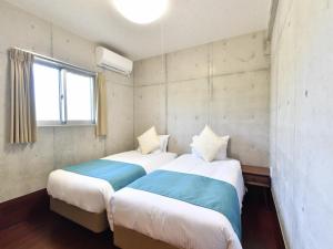 2 Betten in einem kleinen Zimmer mit Fenster in der Unterkunft Churaumi on the Beach Motobu in Motobu