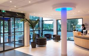 a lobby with a waiting area with a palm tree at Escale Oceania Rennes Cap Malo in La Mézière