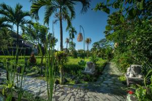 a garden with palm trees and chairs in a yard at Bliss Ubud Spa Resort in Ubud