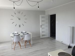 Cette chambre blanche dispose d'une table et d'une horloge murale. dans l'établissement Apartament przy promenadzie, à Ełk