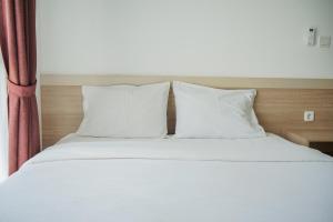 a bed with white sheets and pillows next to a window at Modern and Tranquil 1BR @ Casa De Parco Apartment By Travelio in Tangerang +13 photos