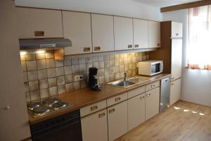 kuchnia z białymi szafkami, zlewem i kuchenką mikrofalową w obiekcie Ferienwohnung Plattner inklusive Sommercard w mieście Jerzens