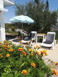 two chairs and an umbrella on a patio with flowers at Apartman ORLOVAC in Slime