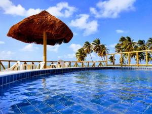 uma piscina com guarda-sol, cadeiras e palmeiras em Pousada Ponta dos Anéis em Maracajaú