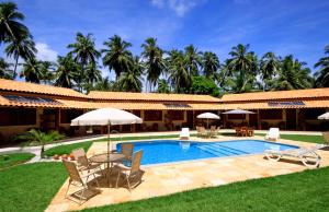 a resort with a swimming pool with chairs and umbrellas at Pousada Yapara-Tyba in Japaratinga