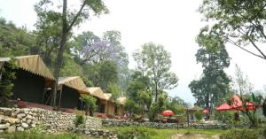 a resort with a stone wall and red umbrellas at Toorani Camps in Uttarkāshi
