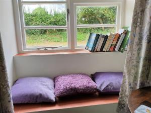a window seat with purple pillows in front of a window at Primrose Cottage in Moreton