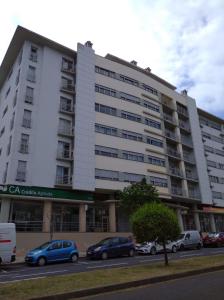 un grand bâtiment blanc avec des voitures garées dans un parking dans l'établissement Duplex Oceanos, à Ponta Delgada
