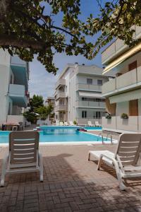 uma piscina com duas cadeiras brancas ao lado de um edifício em Holiday Club Residence em Alba Adriatica