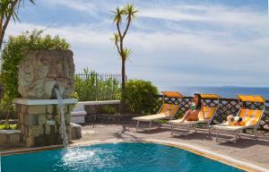 una donna seduta sulle sedie accanto alla piscina di Parco Residence La Rosa a Ischia