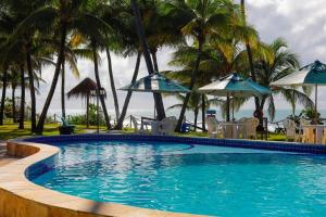 a swimming pool with chairs and umbrellas and the ocean at Pousada Ecoporto in Porto De Galinhas