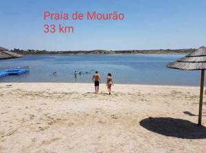 two people walking on a beach near the water at Hotel Passagem do Sol in Moura