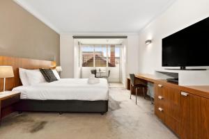 a bedroom with a bed and a desk with a television at Cosmopolitan Hotel Melbourne in Melbourne