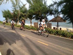 three people riding bikes down a road near the beach at Ruen Thai Rim Haad in Klaeng