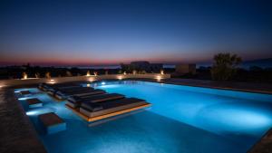 a swimming pool with lounges and chairs at night at Volcanic Arc Suites in Oia