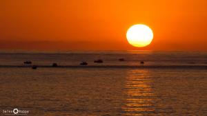 a sunset on the beach with people in the water at La Casetta sul Mare in Isola delle Femmine