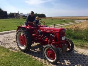 Ein Mann und ein Kind reiten auf einem roten Traktor. in der Unterkunft Ferienhof Schild FeWo Bullerbü in Wangerland