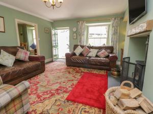 sala de estar con sofás de cuero y alfombra roja en Anvil Cottage en Near Sawrey
