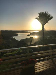 um pôr-do-sol sobre um lago com um banco e uma palmeira em Baywaterviews em Paihia
