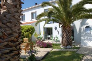 a palm tree in front of a white house at Hotel Le Goeland in Barbâtre