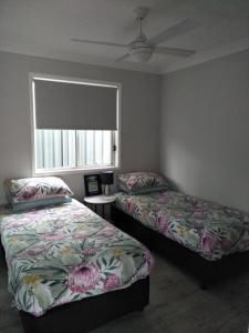 a bedroom with two beds and a window with a fan at Ashley's Retreat Umina Beach in Umina