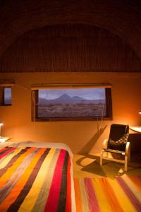 1 dormitorio con 1 cama, 1 silla y 1 ventana en Planeta Atacama Lodge, en San Pedro de Atacama