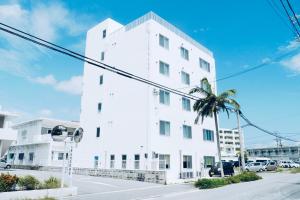 um edifício branco com uma palmeira em frente em ホテルサンドリバー石垣島 em Ishigaki Island