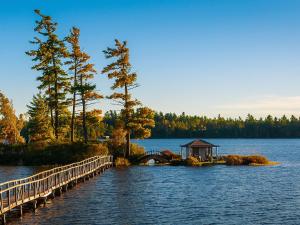 a small island in the middle of a lake with a bridge at White Pine Camp in Paul Smiths