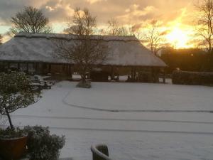 una casa cubierta de nieve con la puesta de sol en el fondo en Cotenham Barn, en South Walsham