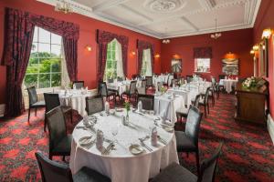 uma sala de jantar com mesas e cadeiras brancas e paredes vermelhas em The Greenhill Hotel em Wigton