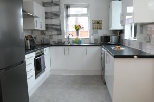 una cocina con armarios blancos y encimeras negras en Ideal Lodgings in Bury - Whitefield en Bury