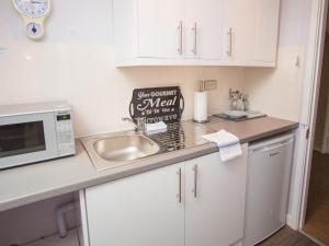 a kitchen with white cabinets and a sink and a microwave at James' Place at Brynawel in Merthyr Tydfil