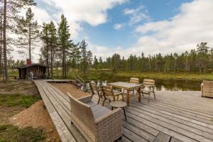 eine Holzterrasse mit einem Tisch und Stühlen neben einem See in der Unterkunft Kuukkeli Log Houses Villa Aurora "Pupula" in Saariselkä