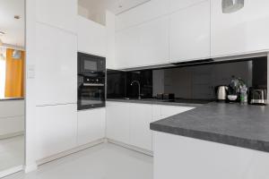 a white kitchen with white cabinets and black appliances at Wilanów Gardens with Balcony in Warsaw