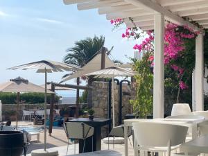 a patio with white tables and chairs and umbrellas at Ostraco Suites in Mikonos
