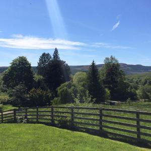 a wooden fence in a field with trees and hills at Leny Estate in Callander