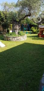 a playground in a park with a tree and a swing at Hotel Maria in Chrysi Ammoudia