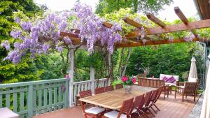 une table et des chaises en bois sur une terrasse avec des glycines violets dans l'établissement L'OURSERIE Bed & Breakfast, à Saint-Paul-en-Chablais