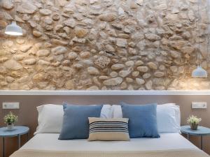 pared de piedra sobre una cama con almohadas azules en Hostal Altea House, en Altea