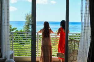 Dos mujeres de pie en un balcón con vistas al océano en Odysis Onna Resort Hotel en Onna