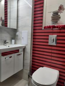 La salle de bains est pourvue de toilettes blanches et d'un mur rouge. dans l'établissement White Apartment, à Kazanlak