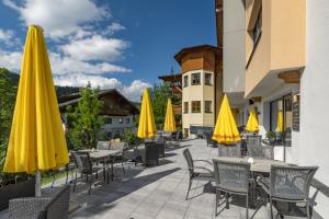 eine Terrasse mit Tischen, Stühlen und gelben Sonnenschirmen in der Unterkunft Wanderhotel Erika in Wagrain