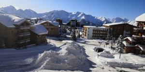 una ciudad cubierta de nieve con montañas en el fondo en La Dauphinoise Alpe d'Huez en L'Alpe-d'Huez