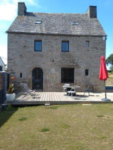 a building with a deck and a table and a red umbrella at Les charmantes pierres percées in Ploumilliau