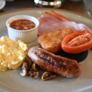 a plate of breakfast food with sausage eggs bacon and mushrooms at Kentisbury Grange in Kentisbury