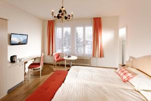 
a room with a bed, chair, table and window at Hotel Beausite in Interlaken
