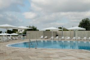 a swimming pool with white chairs and umbrellas at Elma Hotel and Art Complex in Zikhron Ya'akov