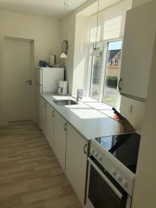 a white kitchen with a sink and a refrigerator at Vemmingbundvejens Ferielejlighed in Broager