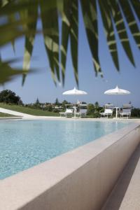 uma piscina com cadeiras brancas e guarda-sóis em Il Borghetto Creative Resort em Tropea