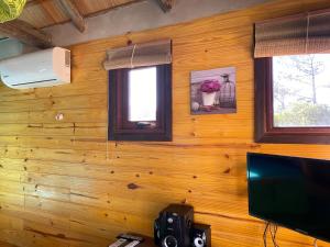 a room with a wooden wall with a television and windows at caribe in Punta Del Diablo